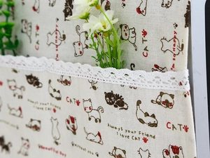 Detail of linen microwave cover with cute cat patterns and white lace edges