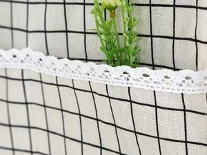 Detailed close-up of linen fabric with black grid pattern and white lace trim detail