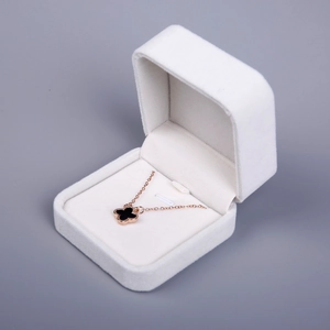 White velvet jewelry box displaying a rose gold black clover necklace on gray background