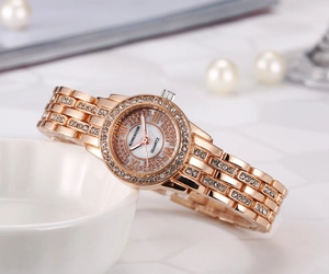 Close-up of rose gold ladies watch featuring a shimmering shell dial and crystal-set strap.