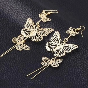 Detailed macro view of golden hollow butterfly dangle earrings with long metal bar tassels