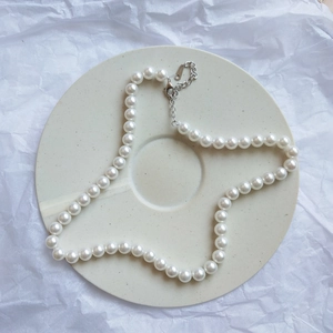Detailed shot of 925 silver pearl necklace with lobster clasp on beige ceramic tray