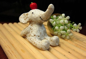 Close-up of a mini ceramic white elephant figurine with a red apple on its head