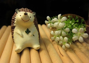 Close-up of a resin hedgehog figurine holding a lucky four-leaf clover on a bamboo mat