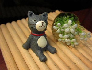 Detail of miniature grey resin cat figurine with red collar sitting on a bamboo mat