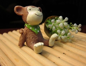 Miniature resin monkey figurine wearing a green polka dot scarf on a bamboo mat