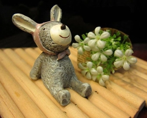 Close-up of a mini resin bear ornament with a pink hat sitting on a bamboo mat with flowers