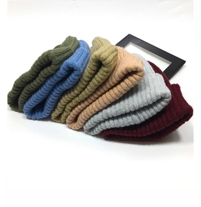 Detailed view of stacked knitted beanies in dark green, blue, yellow, and red colors
