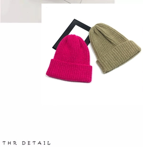 Detail view of pink and olive green knitted beanies showing premium wool texture