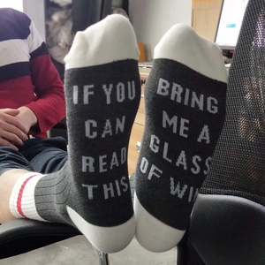 Macro detail of humorous 'Bring Me A Wine' text printed on black cotton crew socks sole