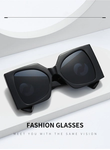 Close-up of oversized black geometric sunglasses with glossy finish on a white podium
