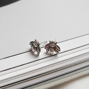Detailed view of sterling silver bee earrings on a lined notebook page with vintage finish