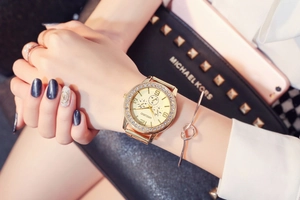 Detailed view of champagne gold watch with rhinestone bezel worn with metallic bracelets