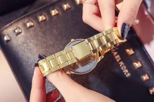 Detail of the golden stainless steel watch band and folding clasp against a black bag