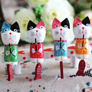 Detail view of four handcrafted wooden fishing cat ornaments in vibrant colors on a white bench