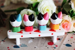 Close-up of four colorful handcrafted wooden fishing cat ornaments on a white bench