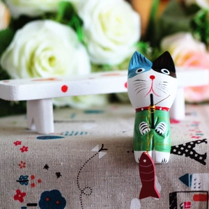 Detailed view of hand-painted wooden fishing cat figurine on a floral fabric surface
