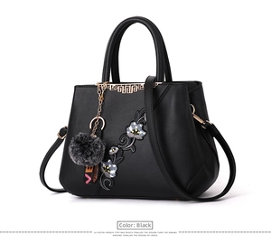 Detail of floral embroidery and fur ball keychain on a black leather handbag