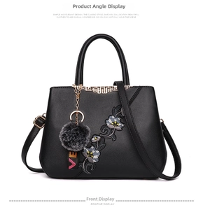 Detail of floral embroidery and gold metal accents on a black faux leather handbag