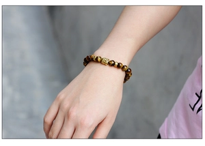 Detailed macro shot of a Tiger Eye beaded bracelet featuring a golden Buddha head bead