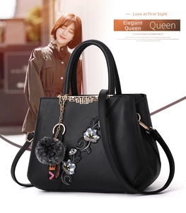 Close-up of floral embroidery on black leather handbag with metallic details and charms