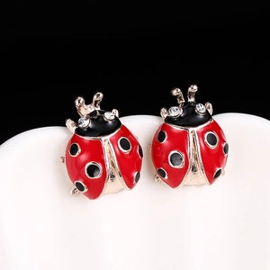 Détail de boucles d'oreilles coccinelles avec émail rouge et cristaux sur fond sobre