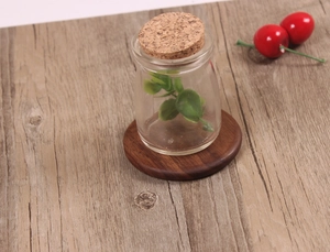Top view of a round black walnut wood coaster supporting a glass bottle and faux plant
