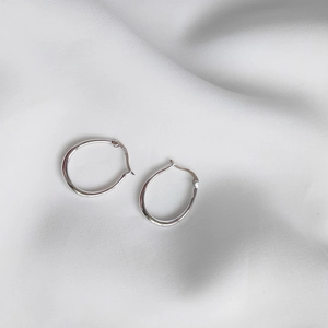Close-up of S925 sterling silver horseshoe earrings on white silk fabric background