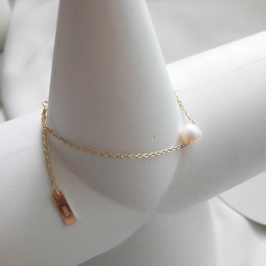 Macro detail of gold S925 silver chain with freshwater pearl on minimalist stand