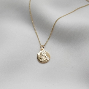 Detailed view of gold Maria pendant with religious relief and Italy hallmark on fine fabric