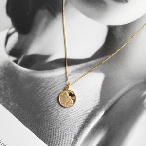 Close-up of golden Virgin of Carmel relief coin pendant and fine metal chain necklace