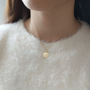 Close-up of a gold Virgin Mary medal necklace worn over a white mohair sweater