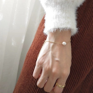 Close-up of minimalist gold chain bracelet with freshwater pearl and ornate ring