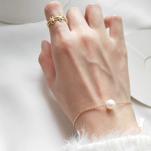Detail of minimalist S925 silver pearl bracelet and gold bow ring on a model