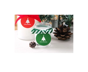 Close-up of Christmas candle jars with red ribbons and merry christmas labels on pine branches