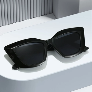 Chic lunettes de soleil œil-de-chat noires oversize avec monture épaisse sur socle blanc