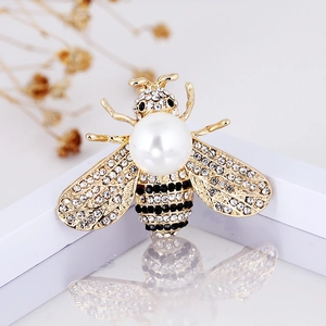 Golden alloy bee brooch with white pearl body and crystal-encrusted wings on white surface