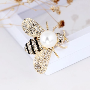 Elegant gold bee brooch with white pearl and sparkling crystals on a minimalist background