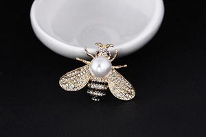 Detailed view of gold alloy bee brooch featuring white pearls and shimmering rhinestones