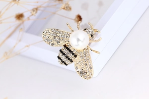 Macro shot of bee brooch with white pearl and rhinestone wings on gold-plated base