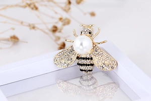 Macro detail of bee brooch with large pearl and sparkling rhinestones on gold base