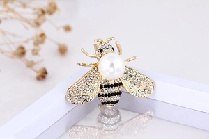 Detailed close-up of a golden bee brooch with white pearls and sparkling rhinestones