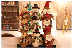 Three plush Christmas dolls featuring Santa, reindeer, and snowman on a wooden table