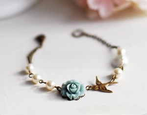 Macro detail of vintage charm bracelet with blue rose, bronze bird, and cream pearls