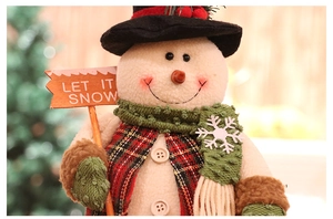 Detail of plush snowman with red plaid jacket and wooden Let It Snow sign