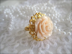 Close-up of pink resin rose ring on golden filigree base with white pearl necklace