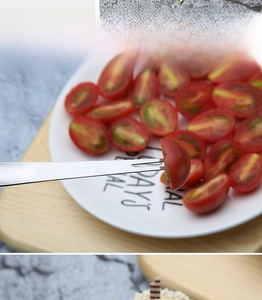 Polished stainless steel two-prong fruit fork picking a tomato on a white ceramic plate