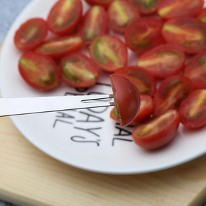 Serrated stainless steel fruit slicer cutting cherry tomatoes on a white ceramic plate