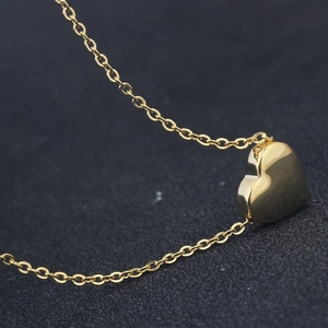 Close-up of a minimalist 18K gold heart pendant necklace on a textured grey background
