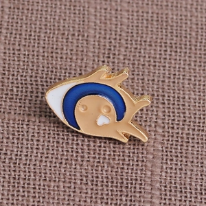 Macro detail of enamel fish brooch with gold plating on a textured burlap background